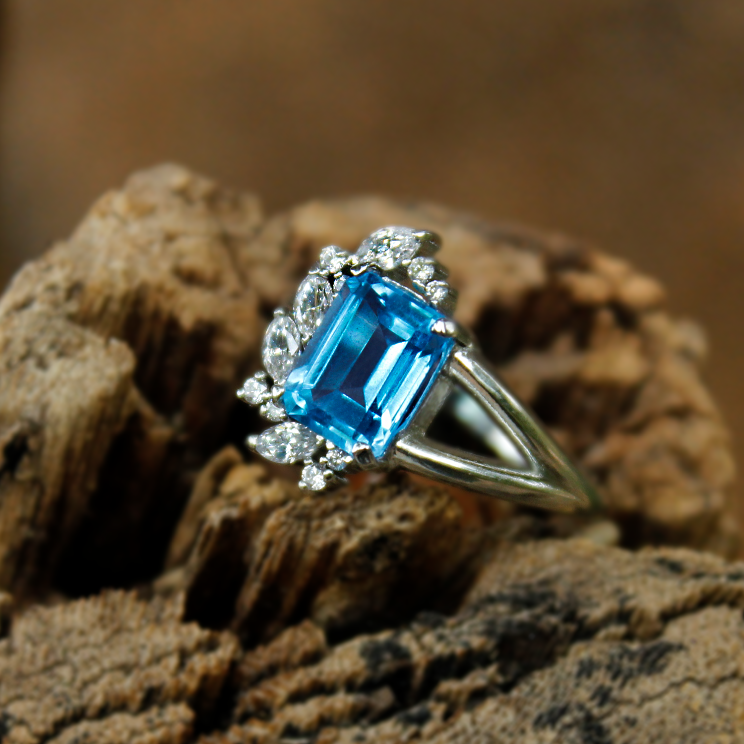 Sterling silver ring with emerald-cut blue topaz and diamond halo displayed on a natural stone surface