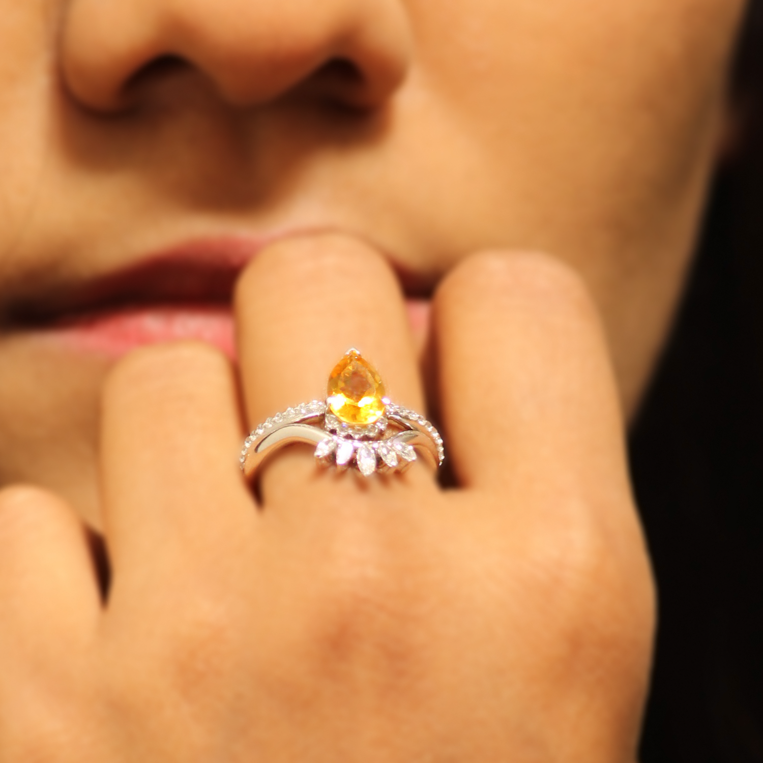 Close-up of a model wearing a silver ring with a vibrant pear-cut Citrine gemstone and marquise accent stones, showcasing elegant design and sparkle.